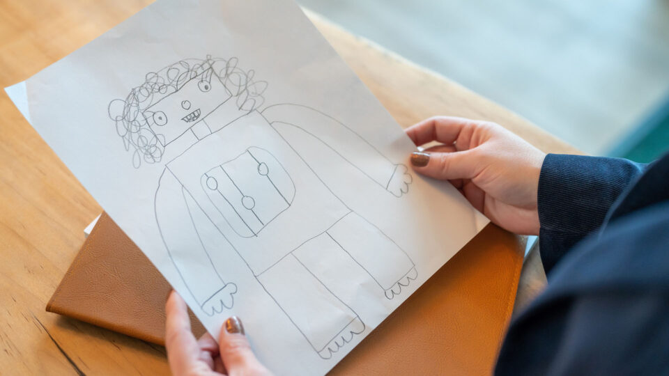 Child's pencil drawing of a robot held by a woman's hands over a wooden table drawn in 2022 as a reminder that even in digital marketing, the human touch matters