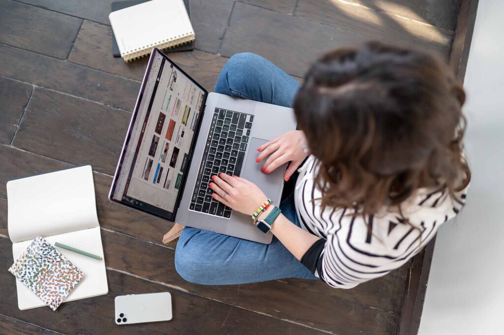 Digital marketing professional working on a MacBook laptop, viewed from overhead, surrounded by notebooks and a smartphone, representing small business online marketing services in Noblesville Indiana